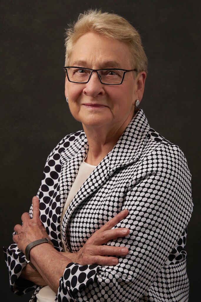 Headshot of Laura Liswood, a White woman with short blondish brown hair, glasses, pearl earrings, and a white and black polka dot suit