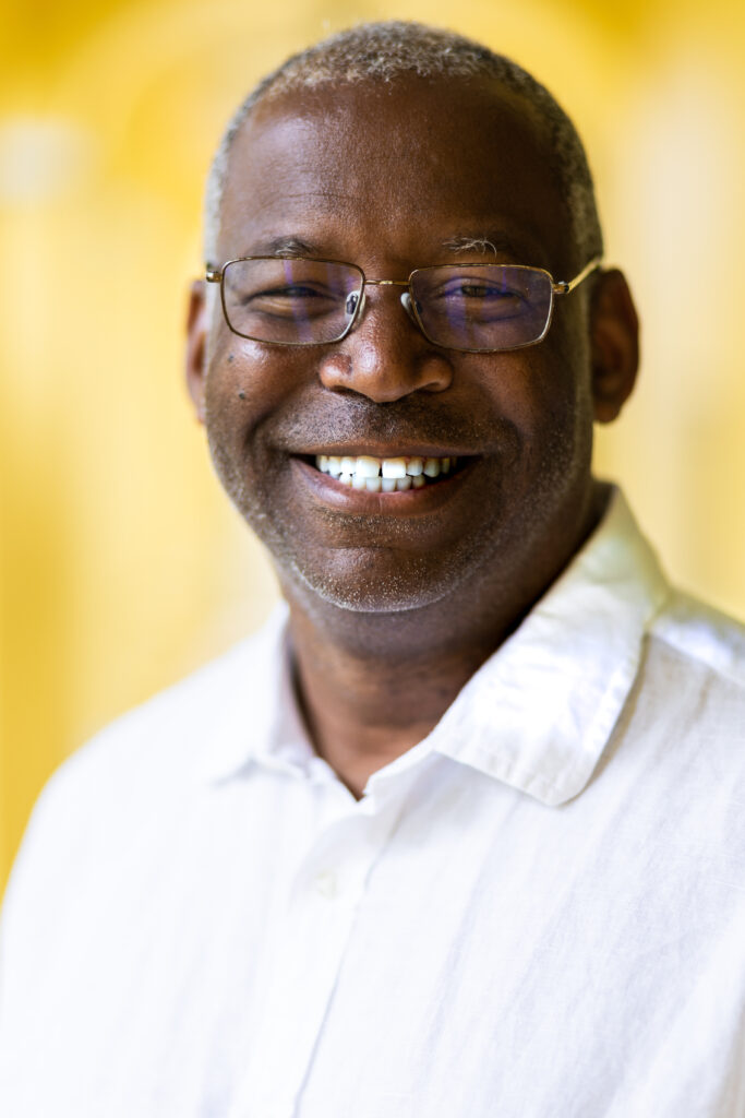 Headshot of William A. Adams, an African American man with short gray hair who is smiling at the camera and wearing thin-framed glasses and a white shirt.