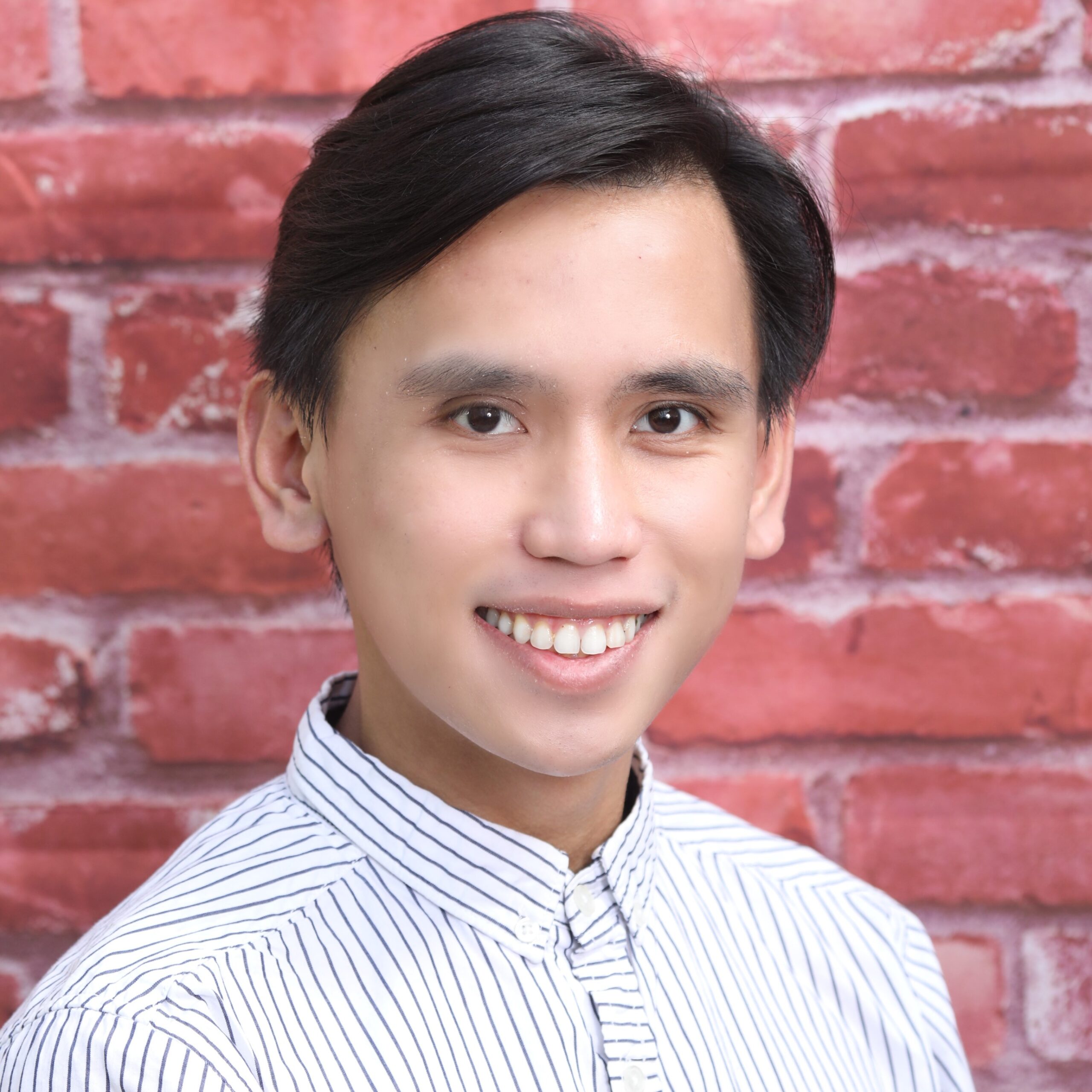 Headshot of Renzo, a Filipino man with short black hair and a white button-down with black pinstripes smiling at the camera in front of a red brick wall