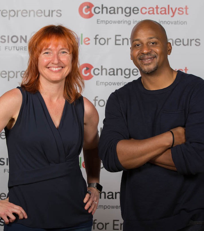 Photo of Melinda, a White woman with red hair and dark blue sleeveless shirt, and Wayne, a bald Black man with a goatee and dark blue long-sleeve shirt, smiling at the camera and standing in front of a step-and-repeat backdrop with Change Catalyst and Google for Entrepreneurs logos